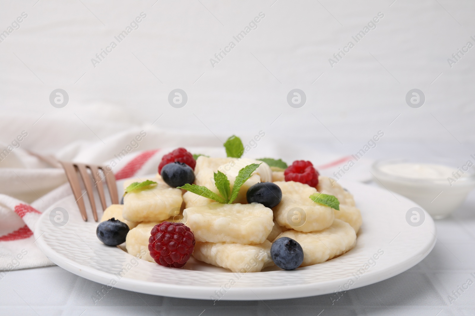 Photo of Plate of tasty lazy dumplings with berries, butter and mint leaves on white tiled table