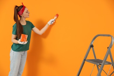 Photo of Happy designer painting orange wall with brush. Space for text