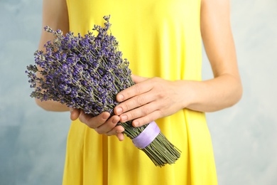 Photo of Woman holding fresh lavender flowers against blue background, closeup view