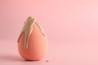 Photo of Makeup sponge with skin foundation on pink background, space for text