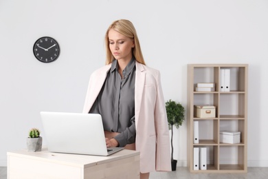 Young woman using laptop at stand up workplace indoors