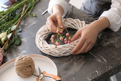 Female florist creating beautiful wreath at table, closeup