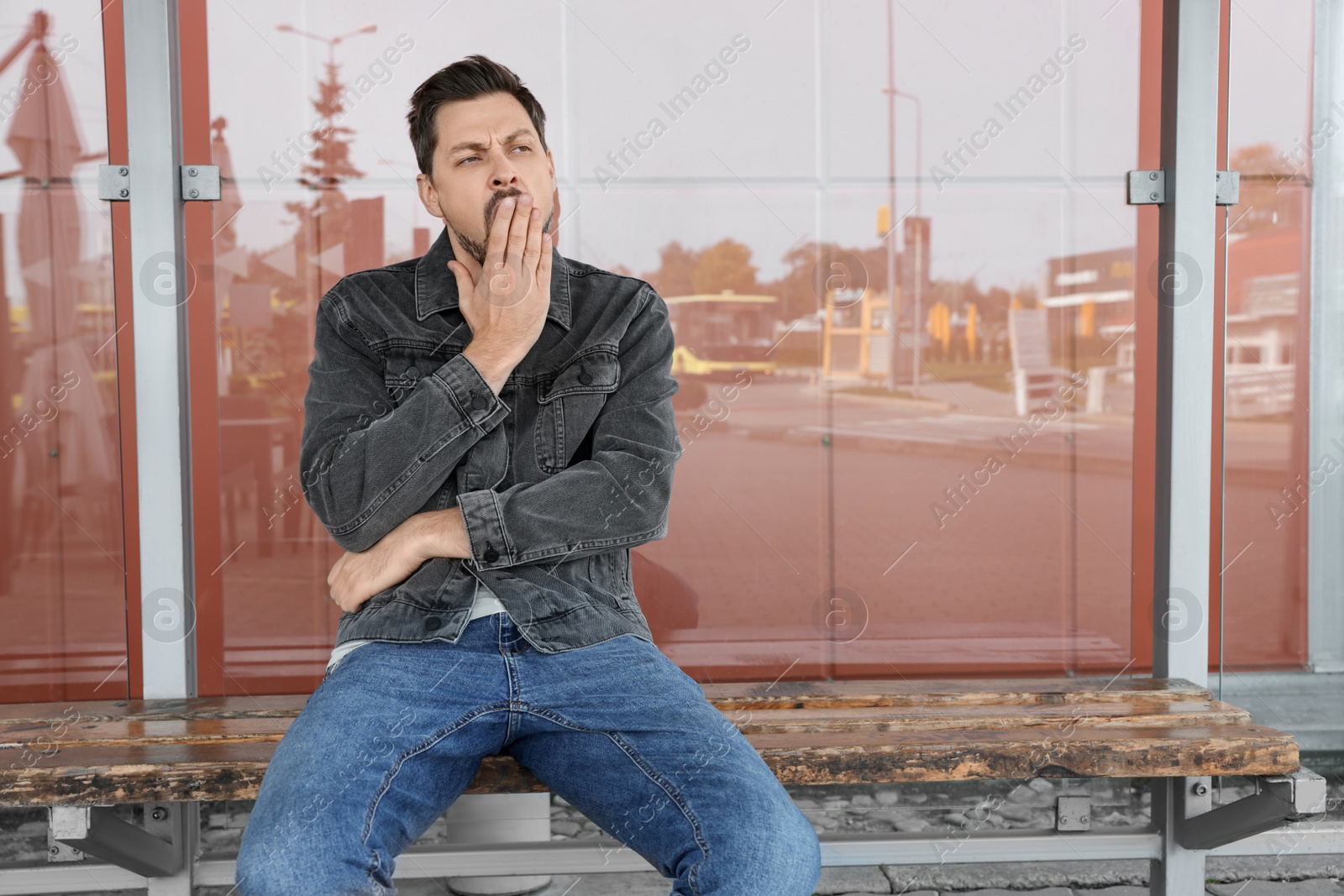 Photo of Sleepy man yawning at public transport stop outdoors. Space for text
