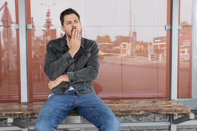 Sleepy man yawning at public transport stop outdoors. Space for text