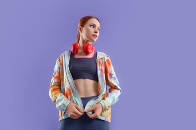 Photo of Young woman in sportswear and headphones on violet background