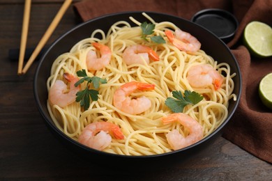 Tasty spaghetti with shrimps and parsley in bowl on wooden table, closeup