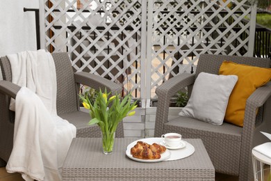 Different pillows, blanket, breakfast and beautiful tulips on rattan garden furniture outdoors