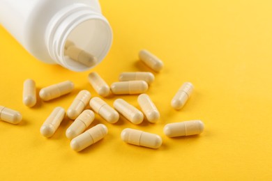 Photo of Bottle and vitamin capsules on yellow background, closeup