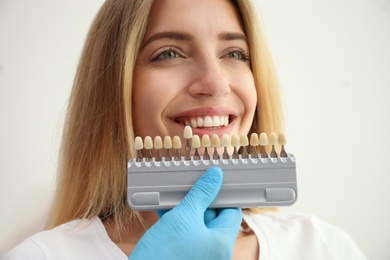 Photo of Doctor matching patient's teeth color with palette on white background, closeup. Cosmetic dentistry