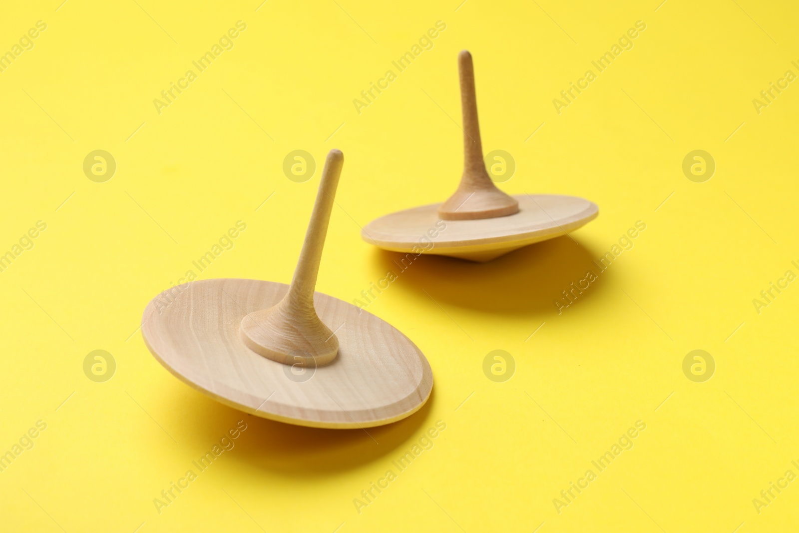 Photo of Two wooden spinning tops on yellow background, closeup