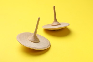 Two wooden spinning tops on yellow background, closeup