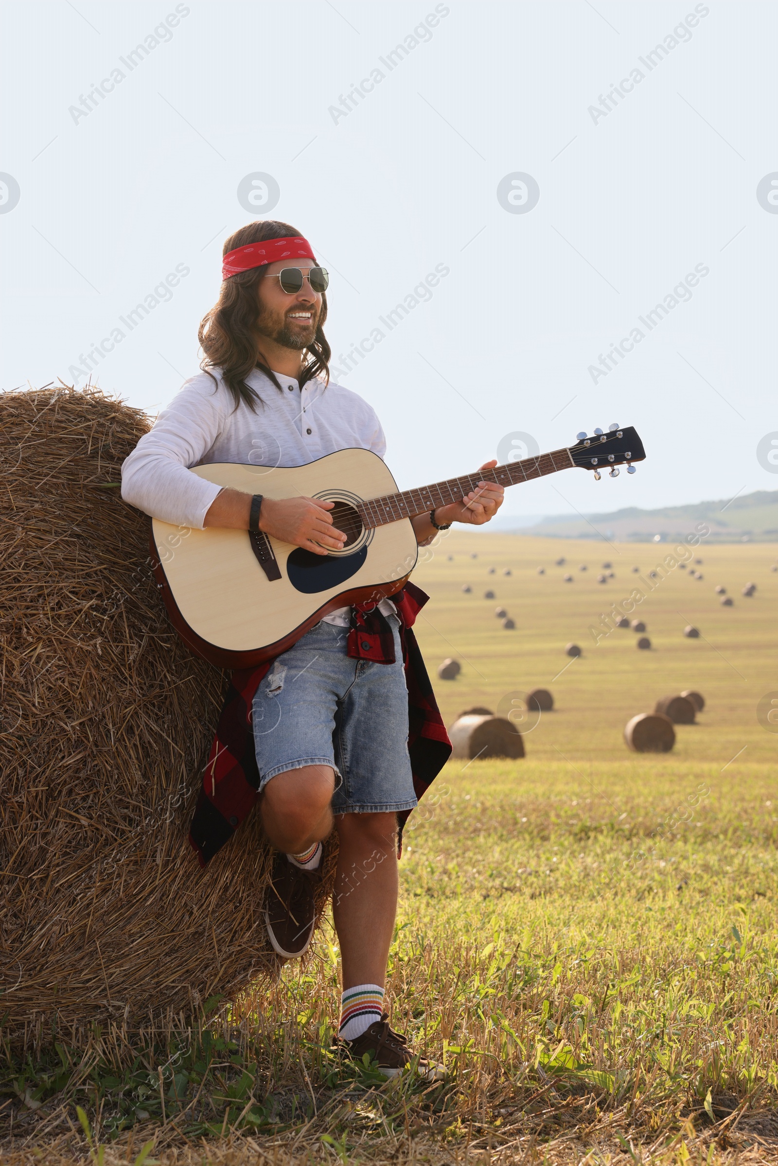 Photo of Hippie man playing guitar near hay bale in field