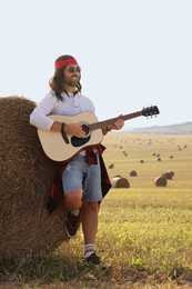 Hippie man playing guitar near hay bale in field