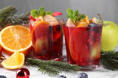 Aromatic Sangria drink in glasses, ingredients and Christmas decor on white marble table