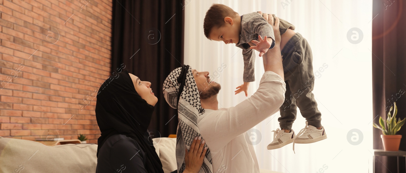 Image of Happy Muslim family spending time together on sofa at home. Banner design 