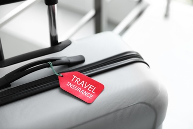 Stylish suitcase with travel insurance label on blurred background, closeup. Space for text