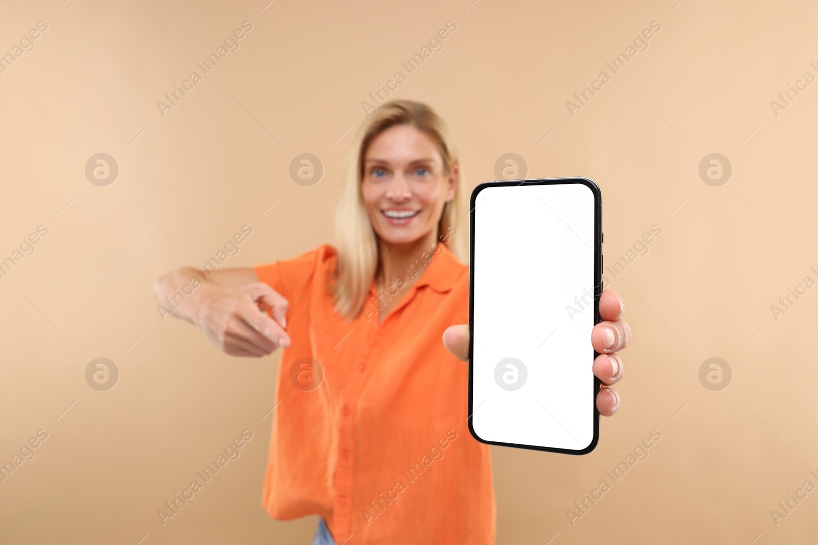 Photo of Happy woman holding smartphone and pointing at blank screen on beige background, selective focus