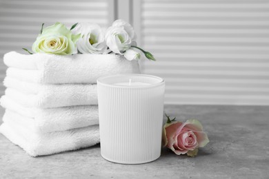 Towels, scented candle and flowers on grey table indoors