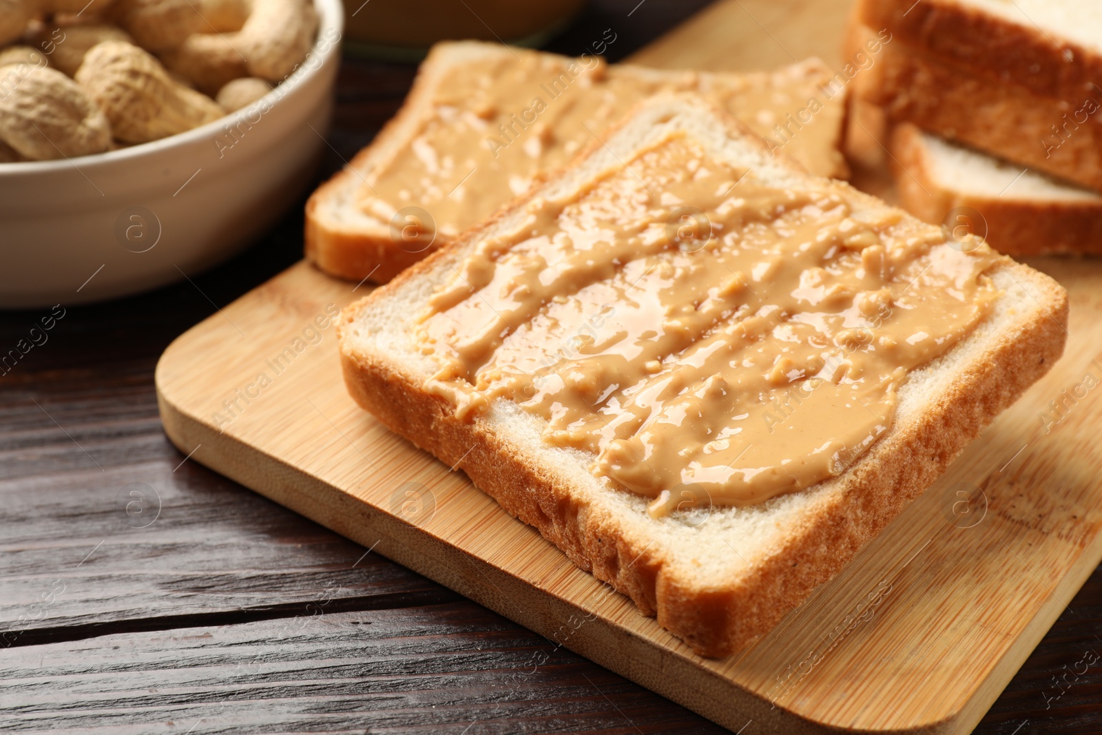 Photo of Delicious toasts with peanut butter on dark wooden table, closeup