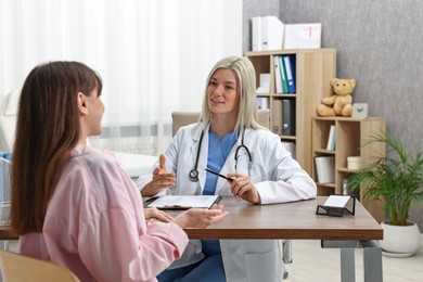 Smiling doctor consulting pregnant patient at table in clinic