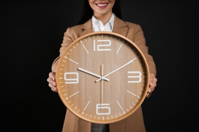 Photo of Businesswoman holding clock on black background, closeup. Time management