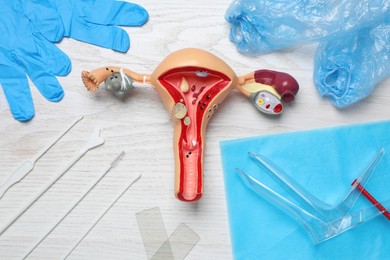 Gynecological examination kit and anatomical uterus model on white wooden table, flat lay