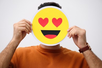 Photo of Man hiding emotions using card with drawn smiling face on white background