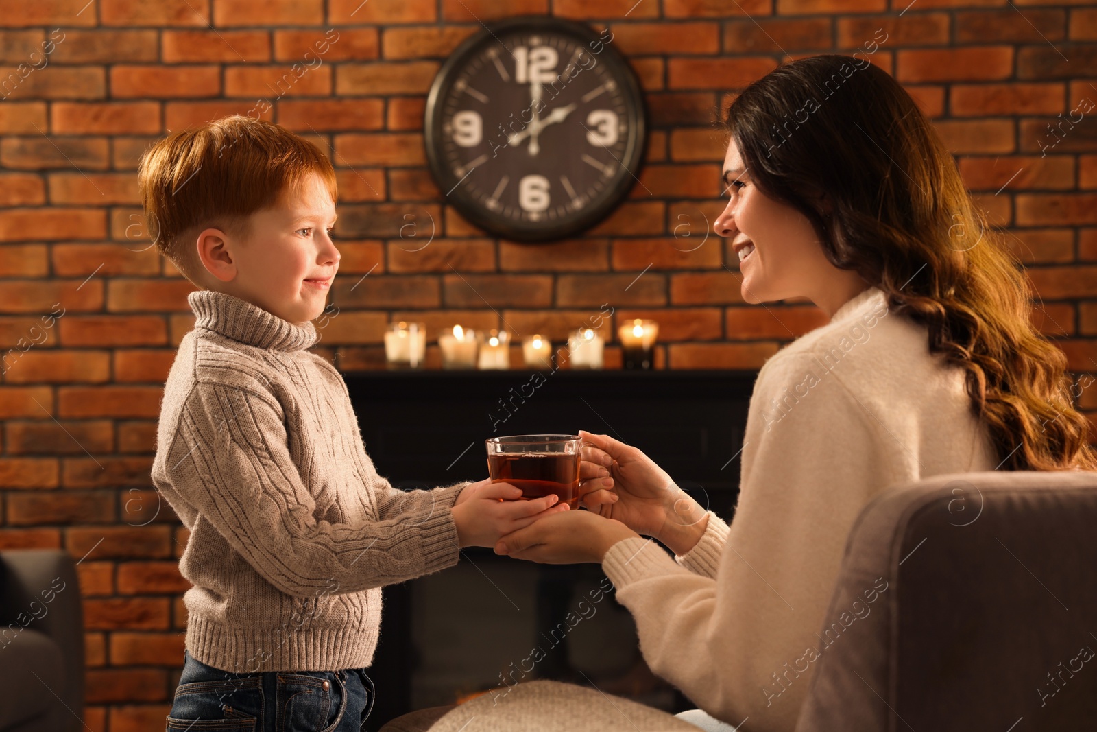 Photo of Mother and son with cup of tea near fireplace at home