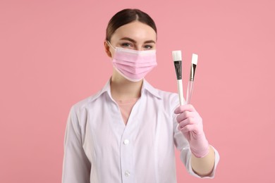 Photo of Cosmetologist with cosmetic brushes on pink background, selective focus