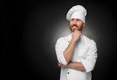 Photo of Smiling mature chef on black background, space for text