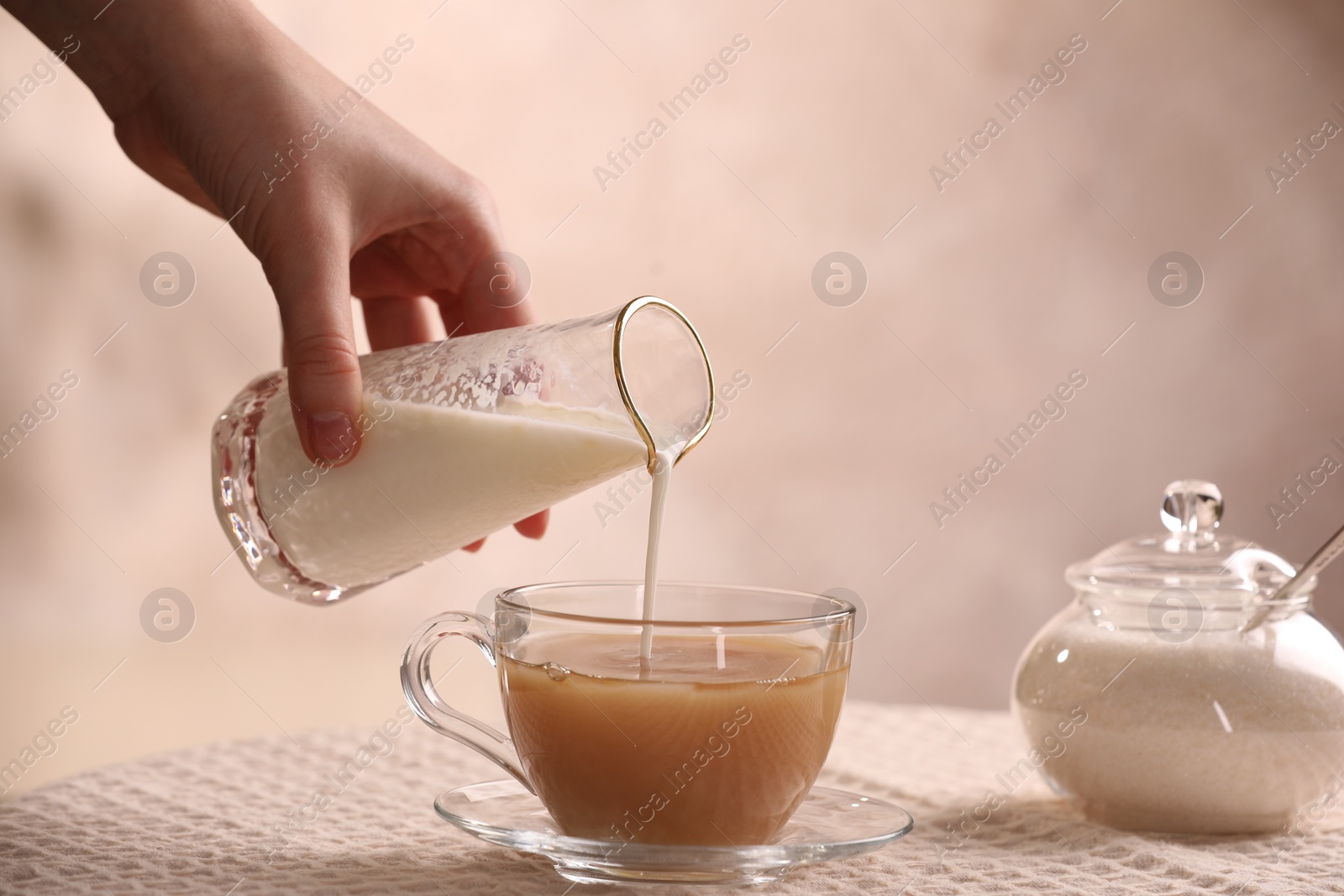 Photo of Woman pouring milk into cup with aromatic tea at table, closeup