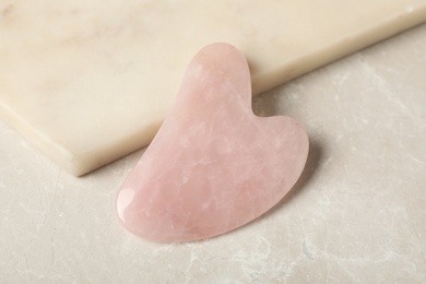 Photo of Rose quartz gua sha tool near board on grey table, closeup