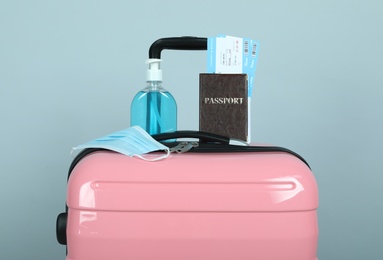 Photo of Composition with passport and protective mask on pink suitcase against light grey background. Travel during quarantine