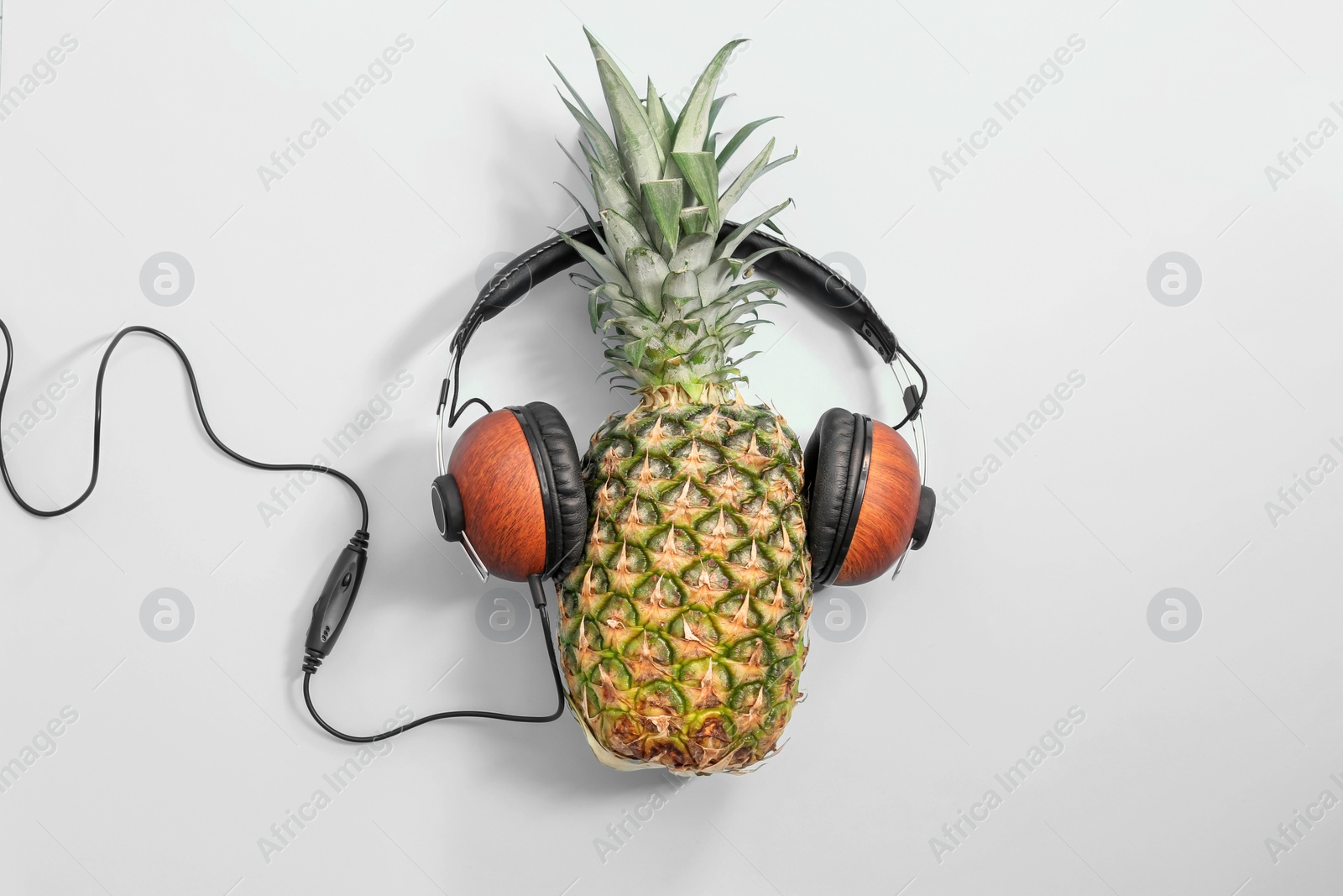 Photo of Fresh ripe pineapple with headphones on color background, top view