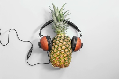 Photo of Fresh ripe pineapple with headphones on color background, top view