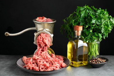 Manual meat grinder with beef mince, spices, oil and parsley on grey table