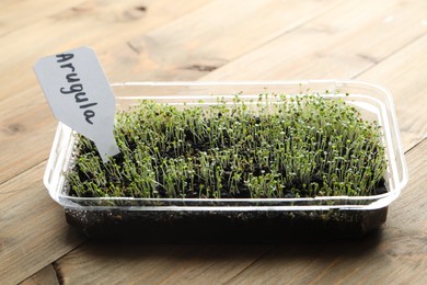 Photo of Young sprouts and card with word Arugula on wooden table