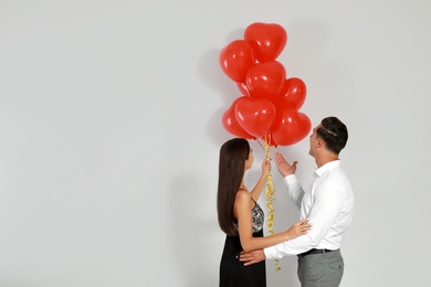 Photo of Beautiful couple with heart shaped balloons on light background, space for text