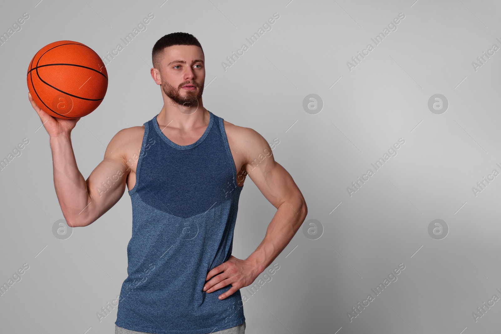 Photo of Athletic young man with basketball ball on light grey background