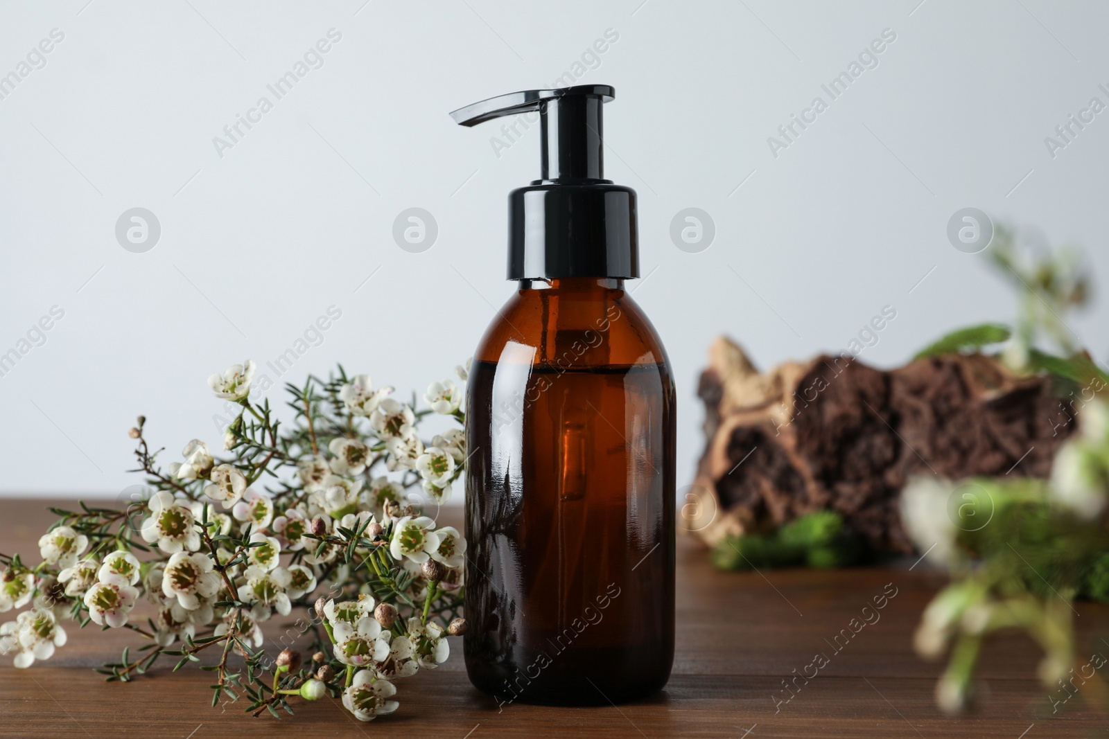 Photo of Bottle of hydrophilic oil and beautiful flowers on wooden table