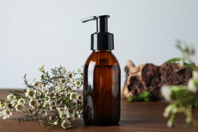 Photo of Bottle of hydrophilic oil and beautiful flowers on wooden table