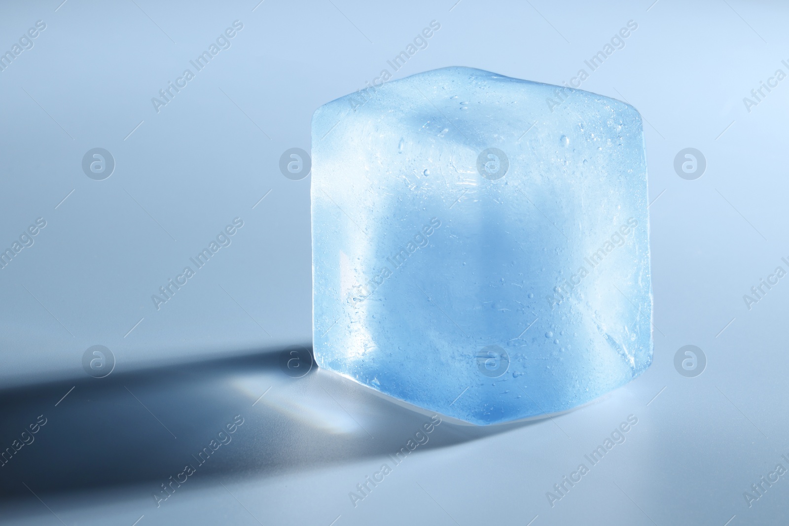 Photo of Crystal clear ice cube on light blue background, closeup. Space for text