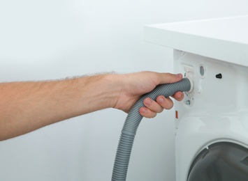 Young plumber fixing washing machine in bathroom, closeup