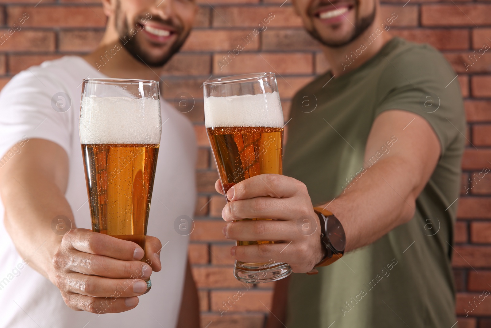 Photo of Friends with glasses of beer near red brick wall, closeup