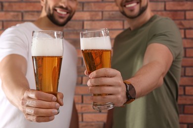 Photo of Friends with glasses of beer near red brick wall, closeup