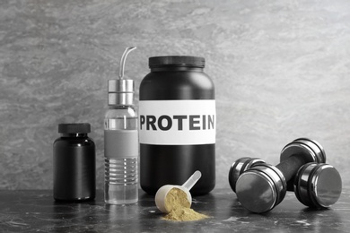 Hemp protein powder in measuring spoon, jars, bottle and dumbbells on table