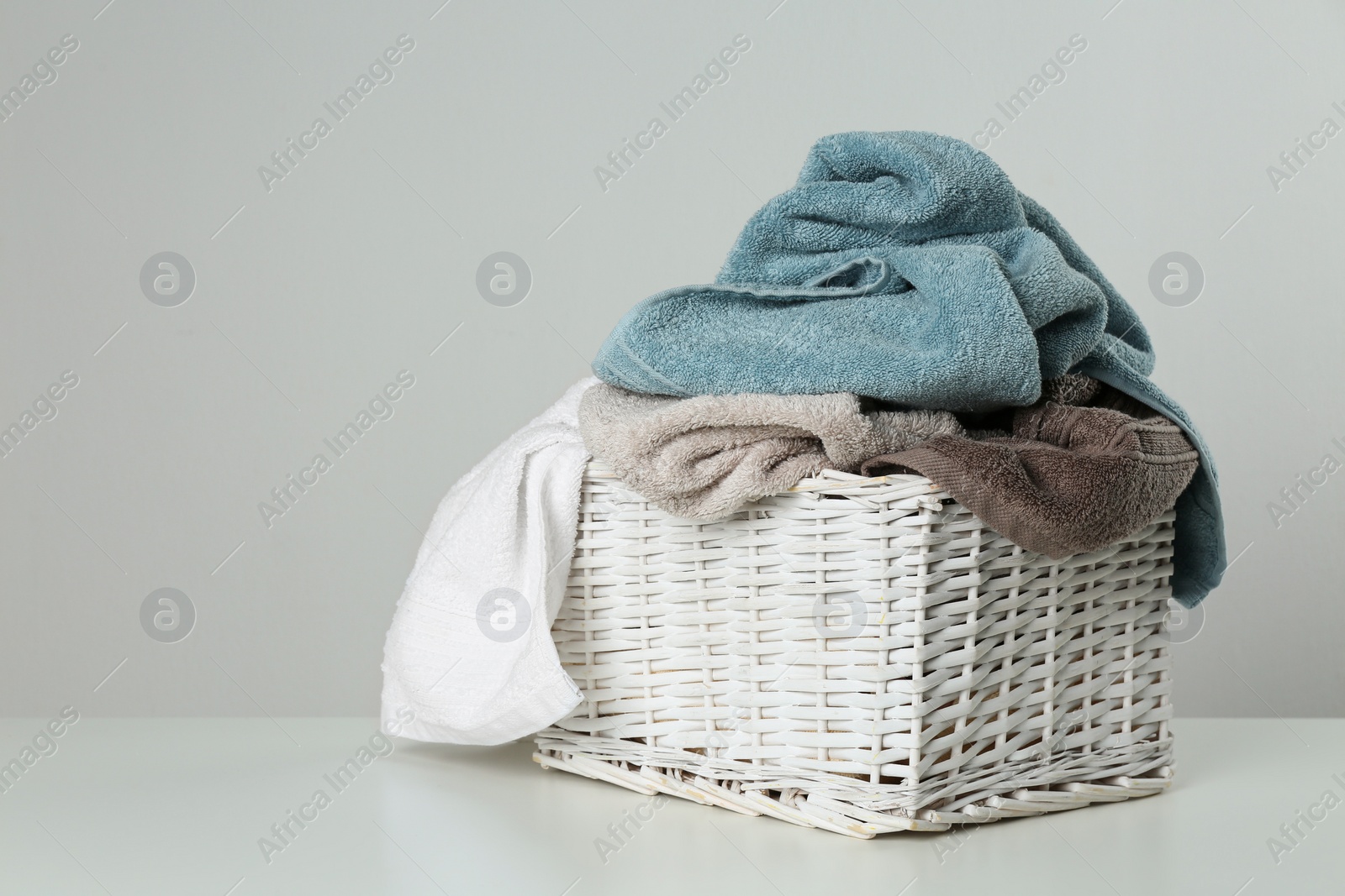 Photo of Wicker laundry basket with towels on light background. Space for text
