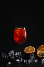 Photo of Glass of tasty Aperol spritz cocktail with orange slices and ice cubes on table against black background, space for text