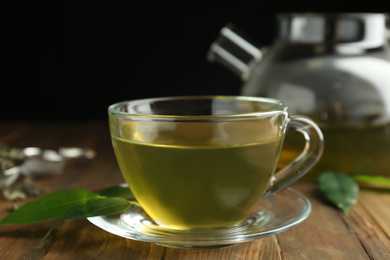 Photo of Cup of aromatic green tea and leaves on wooden table