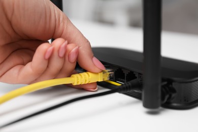 Photo of Woman connecting cable to router at white table, closeup. Wireless internet communication